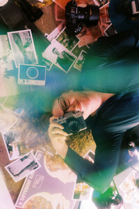 Film photo with light leaks of Allison Bolin Texas wedding photographer laying on the ground with a camera surrounded by printed photos