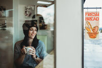 woman looking out of window while holding a white mug