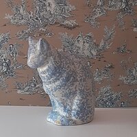a blue and white ceramic cat sitting in front of a wallpapered room
