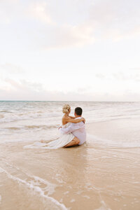 Bride and groom sit on the beach in intimate wedding photo NB CA