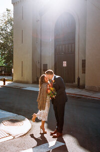 Film photo of a couple kissing outside Providence City Hall, with the bride in a short lace dress and shawl — a golden-hour moment captured by a film wedding photographer.