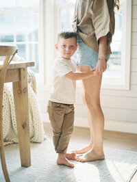 Photo taken from eye level of little boy standing at his mom's feet holding her hand