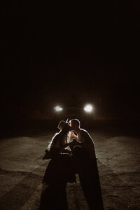 Couple kissing in the headlights surrounded by darkness.