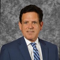 David Sanderson, a white man with dark hair, wears a blue suit & tie with a white shirt in his headshot