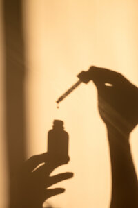 shadow of a hand holding a bottle of serum on a yellow background