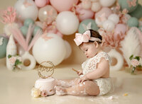 Baby girl eating cake by pastel balloon garland. Photographed by Jenni Nikki at Atlanta Photography studio.