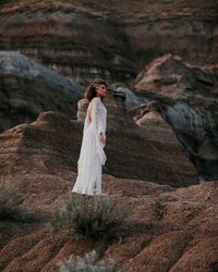 A young bride stands on the edge of a Drumheller hoodo during a Styled bridal photography  photoshoot