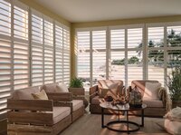 White shutters in a cozy sunroom with a beach view