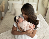 mom holding newborn baby girl wrapped in pink for newborn photoshoot