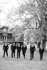 Group of groomsmen in suits walking in a natural setting, black and white photo for a classic timeless look