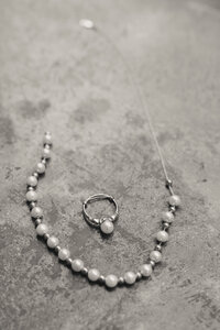 wedding detail image of pearl necklace and peal ring on a cement floor with natural light shining in