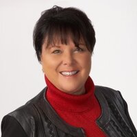 Kathryn, a white woman with dar, short, pixie style hair smiles in her headshot, wearing a black jacket and red shirt