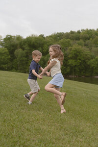 A brother and sister play together in a field of grass next to water and trees at Winged Deer Park in Johnson City TN. Taken by a Northeast TN photographer. 
