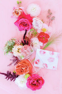 Flat lay of a coupe glass  with pink, orange and white flowers on a pink background