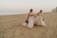 a newlywed couple holding hands and walking across the beach 