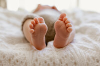 Close-up of tiny newborn baby feet resting on a white knitted blanket during an in-home lifestyle photography session in Las Vegas by Angela Wolf Photography.