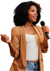 A woman with curly hair, wearing a tan blazer and white top, holds a microphone while gesturing confidently. She appears to be speaking passionately.
