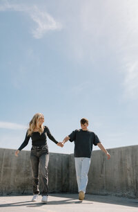 A couple holding hands on top of a parking garage, running together.