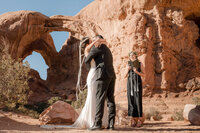 Bride and groom kiss in front of arches national park