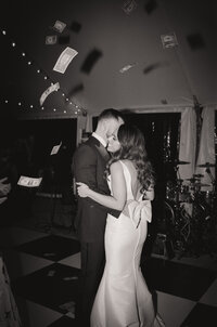 Black and white film photo of a couple sharing a kiss on the dance floor at their Greek wedding at the Stevens Estate, with money falling from above — captured by a film wedding photographer.