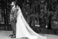 Bride wrapping her arms around the groom from behind in a black and white portrait, capturing an intimate and timeless moment of love and connection.