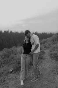 Black and white photo of a man holding his fiancé from behind as she looks up at him smiling.