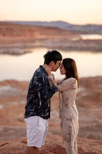 man proposing to his partner on the serene shores of Lake Powell, with towering red rock cliffs and the clear blue water in the background.