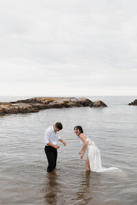 A newlywed couple laughing as they stand in the water 