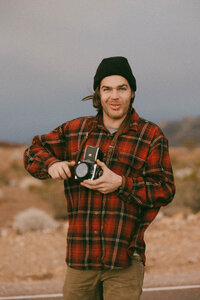 man wearing flannel and holding a film camera in desert