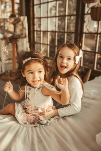 Two beautiful girls explore the square glass windows Mini Session. The older sister graces the scene in a delightful green dress, adorned with a charming white hair bun, while the youngest adds a touch of sweetness in her printed flower dress.
