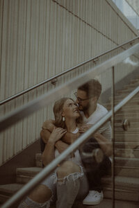 Couple in the city, sitting on stairs while he embraces her from behind.
