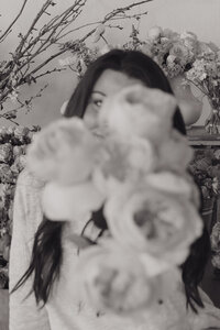 A black and white photo where Michaela holds a bouquet of flowers to the camera in front of her face in a photography studio in Northeast TN 