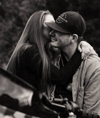 Girl sitting in guy's lap on motorcycle and whispering into his ear