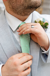 Groom casual straightening his tie while showing off his wedding ring