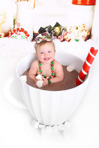 girl smiles in a mug full of hot chocolate at her christmas photoshoot