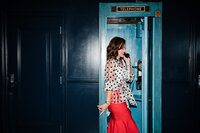 A wedding planner laughs while speaking on a vintage phone, dressed stylishly in polka dots and red, highlighting the charm of Socially Significant Events.