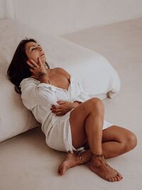 Vrouw zit ontspannen naast bed tijdens boudoirshoot in Oost-Vlaanderen