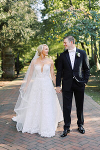 Brittany and Michael share a loving gaze on the grounds of Boxwood Estate. Surrounded by lush greenery, they smile at each other in a tender moment. Brittany wears a beautiful white wedding gown, and Michael is dressed in a sharp suit. The soft natural light highlights the couple's connection, creating a romantic and intimate atmosphere on their special day.