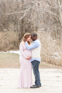 A pregnant woman and her husband stand close during winter photos