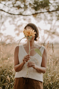 Woman standing in a field holding a sunflower in front of her face 