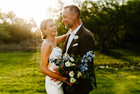 bride and groom holding each other smiling with sunset sun flair behind them