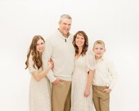 Family standing close together by a wall in a white studio at Jennifer Hall Photography, LLC in North East, PA.