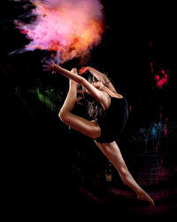 A young woman leaps through the air as bright oranges and pinks burst above her.