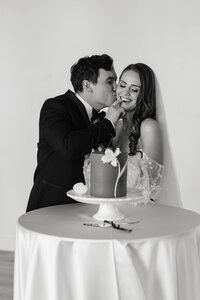 bride and groom kissing sweetly behind their wedding cake in black and white