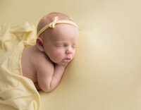 Newborn baby with headband on yellow fabric