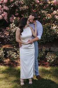 Romantic couple embracing at the Portland Rose Garden, surrounded by blooming pink roses and lush greenery, captured in a vibrant and intimate Pacific Northwest wedding photography session.