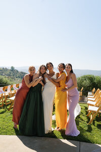 Four bridesmaids and the bride laughing and posing together in colorful dresses at an outdoor Southern California private estate wedding on a sunny day.