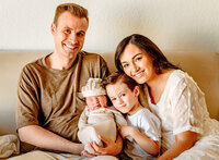 Family snuggling newborn on the couch. Captured by Cactus & Pine Photography