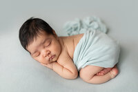 Newborn boy wrapped in egg shell blue color  during his first portrait session.