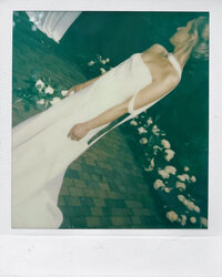 A bride stands in a garden surrounded by flowers in a polaroid